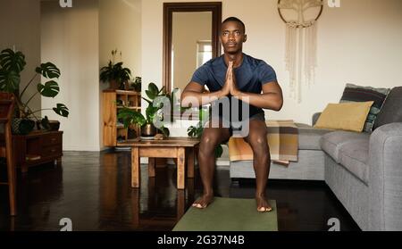 L'uomo africano nella sedia posa mentre facendo yoga a casa Foto Stock