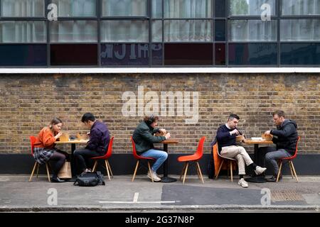 Persone che siedono a mangiare ai tavoli social distancing a pranzo in Leather Lane Street Market Londra Inghilterra UK 2021 KATHY DEWITT Foto Stock