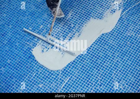 Lavoratore che copre le fiamme sulla piastrella in piscina. Lavori di riparazione della piscina Foto Stock