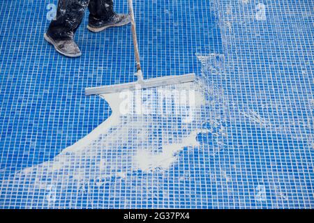 Lavoratore che copre le fiamme sulla piastrella in piscina. Lavori di riparazione della piscina Foto Stock