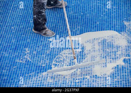 Lavoratore che copre le fiamme sulla piastrella in piscina. Lavori di riparazione della piscina Foto Stock