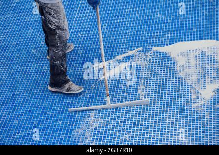 Lavoratore che copre le fiamme sulla piastrella in piscina. Lavori di riparazione della piscina Foto Stock