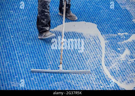 Lavoratore che copre le fiamme sulla piastrella in piscina. Lavori di riparazione della piscina Foto Stock