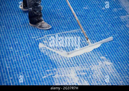 Lavoratore che copre le fiamme sulla piastrella in piscina. Lavori di riparazione della piscina Foto Stock