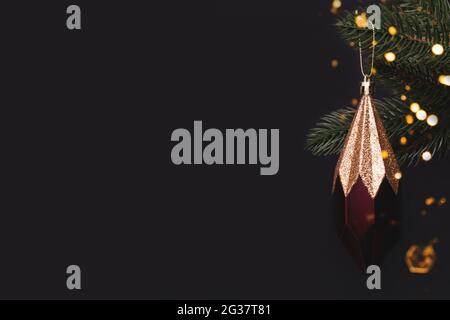 Scintillante icicola natalizia appesa su un ramo di abeti. Decorazione di Capodanno di fronte a sfondo nero con spazio per la copia. Foto Stock