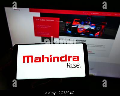 Persona che tiene il cellulare con il logo della società automobilistica indiana Mahindra Mahindra Limited sullo schermo di fronte alla pagina web. Mettere a fuoco il display del telefono. Foto Stock