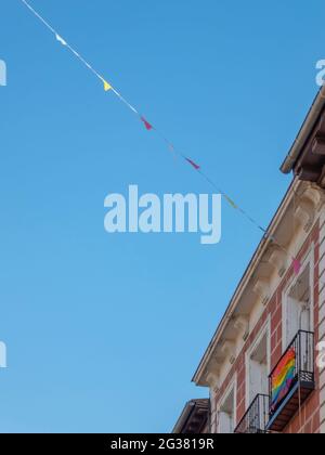 I pennants della fiera appesi fra i balconi con la bandiera del Pride gay nella strada in una giornata estiva soleggiata Foto Stock