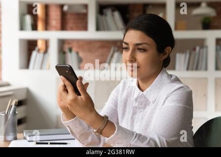 Giovane donna indiana manager che utilizza l'applicazione per smartphone. Foto Stock