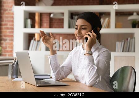 Felice giovane donna indiana multitasking in ufficio moderno. Foto Stock
