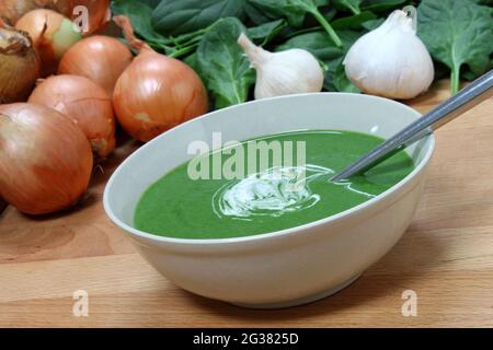 Una ciotola nutriente di zuppa di spinaci freschi, con alcuni degli ingredienti dietro. Foto Stock