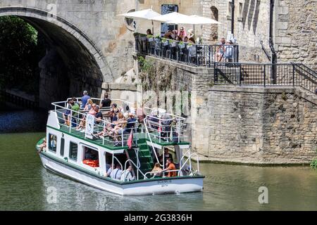 Bath, Regno Unito, 14 giugno 2021. Con molte parti del Regno Unito che godono di un'altra giornata molto calda e soleggiata, le persone che gustano un pasto all'aperto accanto al fiume Avon osservano mentre una barca passa sotto il ponte Pulteney. Credit: Lynchpics/Alamy Live News Foto Stock