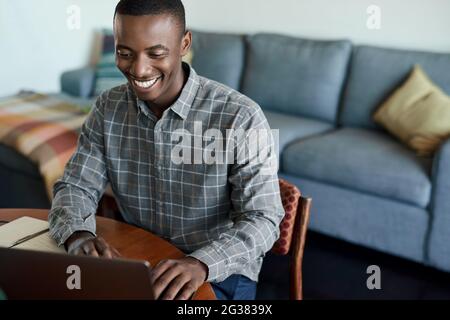 Sorridente giovane uomo d'affari africano che lavora su un computer portatile a casa Foto Stock