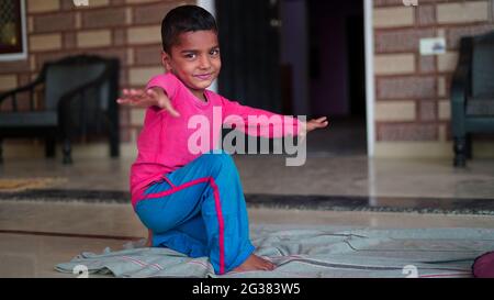 Yoga bambini. Piccolo ragazzo indiano facendo esercizio di yoga e guardando le istruzioni in TV. Concetto di giornata di yoga in tutto il mondo. Foto Stock