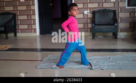 Indiano piccolo ragazzo carino che si esercita a casa. La famiglia lavora a casa. Concetto di giornata di yoga in tutto il mondo. Foto Stock