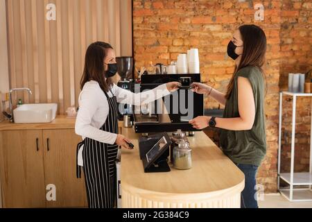 Donna caucasica proprietario di affari e cliente che indossa maschere facciali, prendendo ordine Foto Stock