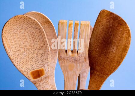 Utensili da cucina in legno usati come cucchiaio, spatola e forchetta su sfondo blu. Foto Stock