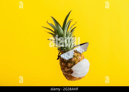 Faccia fredda su ananas in occhiali protettivi maschera medica da sole. Levitating frutta tropicale di ananas isolata su sfondo giallo estivo. Minimalista Foto Stock
