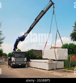 Un camion con gru telescopica consegna pacchi contenenti un blocco di legno (abete), una casa di legno pretagliata che viene montata sul posto. Udine Provin Foto Stock