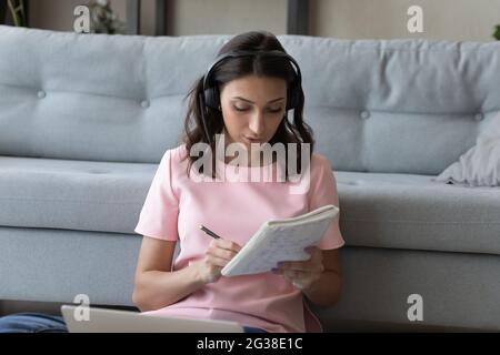 Primo piano donna araba concentrata in cuffie prendere appunti Foto Stock
