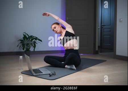 Durante l'auto-isolamento, la ragazza prende una lezione di yoga a casa, esegue esercizi di stretching. Foto Stock