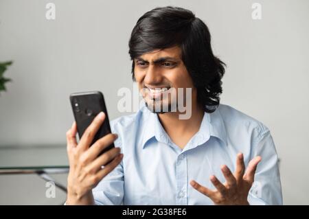 Infastidito imprenditore indiano sta fissando lo smartphone, ritratto di delusione orientale maschio dipendente tenere smartphone, ha fallito conversazione telefonica, negoziazione fallita, ha ricevuto cattive notizie Foto Stock