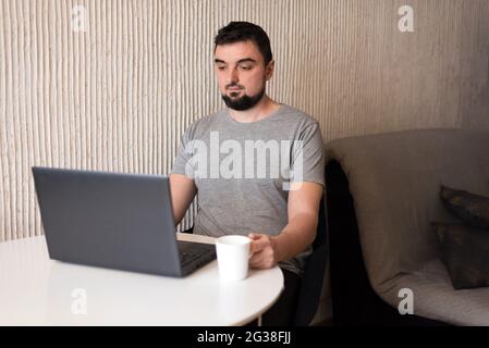 Giovane professionista maschile che utilizza il computer seduto alla scrivania di casa. Freelance occupato che lavora a casa Foto Stock