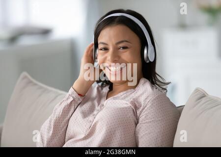 Donna Happy Black che indossa le cuffie, riposandosi sul divano Foto Stock