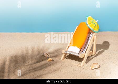Composizione creativa con crema solare su una sedia a sdraio giocattolo sulla sabbia con conchiglie e ombra foglia di palma. Concetto di vacanza estiva. Sfondo estivo. Foto Stock