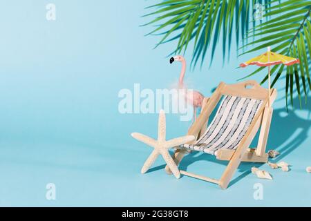 Composizione creativa con accessori da spiaggia, come sdraio, ombrellone, conchiglie, fenicotteri rosa e foglia di palma su sfondo blu. Vacanza estiva Foto Stock
