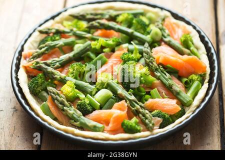 Preparazione di quiche con salmone, broccoli e asparagi verdi, ricoperti di latte e uova. Crostata grezza - forno pronto. Foto Stock
