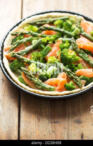 Preparazione di quiche con salmone, broccoli e asparagi verdi, ricoperti di latte e uova. Crostata grezza - forno pronto. Foto Stock
