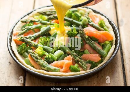 Preparazione di quiche con salmone, broccoli e asparagi verdi, ricoperti di latte e uova. Crostata grezza - forno pronto. Foto Stock