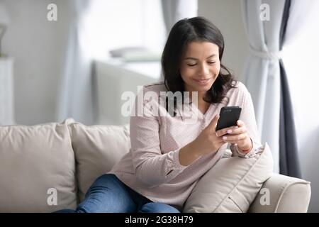 Felice giovane donna millenaria con smartphone rilassante sul divano Foto Stock