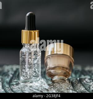 Skincare cosmetic Serum flacone con fluido collagene acido ialuronico, crema idratante vaso su acqua gel bolle superficie texture. Acqua d'oro di lusso Foto Stock