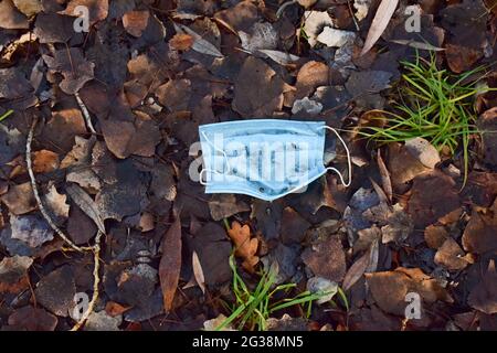 Usato maschera medica di protezione blu sporca si trova gettato sul fogliame autunnale a terra Foto Stock