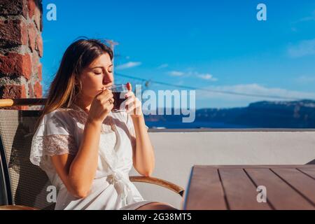 Donna che si rilassa sulla terrazza dell'hotel bevendo il caffè del mattino godendo del paesaggio di montagna e mare. Vacanze estive Foto Stock