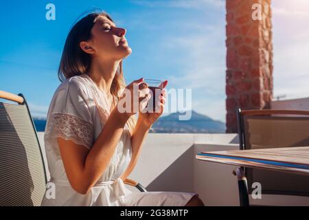 Donna che si rilassa sulla terrazza dell'hotel sorseggiando un caffè del mattino godendo del paesaggio montano di Santorini ad Akrotiri. Vacanze estive Foto Stock