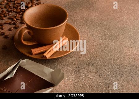 Tazza vuota di ceramica con piattino, cannella, chicchi di caffè sparsi e cioccolato su una superficie di pietra Foto Stock