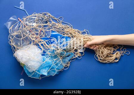 Mano umana con immondizia in rete di pesce su sfondo colorato. Concetto di ecologia Foto Stock