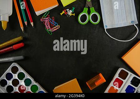 Ritorno a scuola, istruzione. Torna a scuola sulla lavagna nera della scuola. Matite di sfondo, vernici, visiera, graffette. Vista dall'alto. Copia Foto Stock