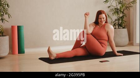 Donna seguendo le istruzioni sul cellulare mentre si fa yoga. Donna che guarda il telefono cellulare mentre si pratica yoga stretching allenamento. Foto Stock