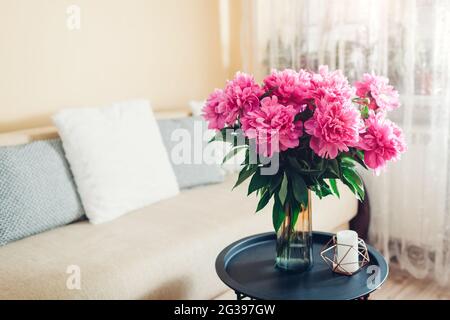 Interni e arredamento domestico. Fiori freschi di peonie rosa messi in vaso in soggiorno da divano. Bouquet di fiori sul tavolino da caffè Foto Stock