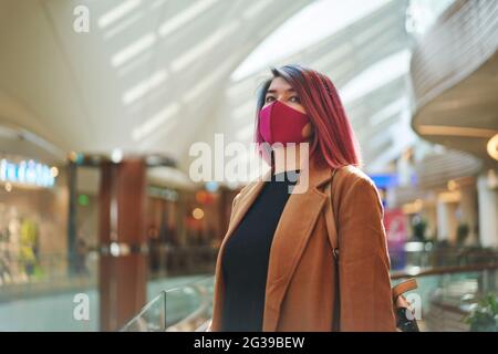 Donna con capelli rosa che indossa la maschera facciale nel centro commerciale. Foto Stock