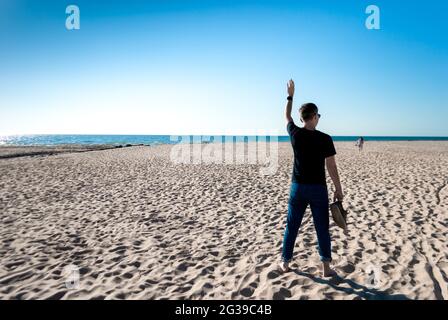 L'uomo sulla spiaggia ondeggia la mano a una donna che cammina in lontananza Foto Stock