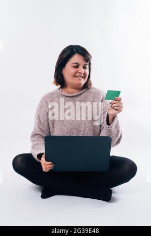 Immagine verticale di una donna seduta guardando una carta di credito e utilizzando un personal computer. Concetto di shopping su Internet Foto Stock