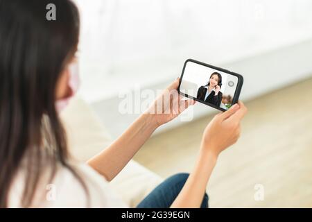 la giovane donna indossa una maschera per proteggersi a casa e utilizza le videochiamate con i colleghi dell'azienda Foto Stock