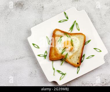 Uovo in un buco toast con pepe nero e cipolle verdi su una piastra rettangolare bianca su uno sfondo grigio chiaro. Vista dall'alto, disposizione piatta Foto Stock