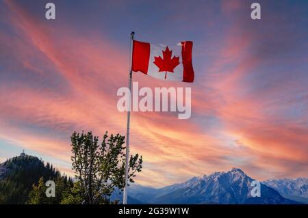 Bandiera canadese che vola sulla cima della Sulphur Mountain con vista al tramonto del Parco Nazionale di Banff con le Montagne Rocciose canadesi sullo sfondo. Foto Stock