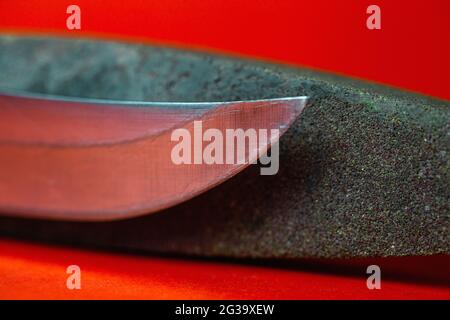 affilatura dei coltelli e pietra per affilare i coltelli su fondo rosso Foto Stock