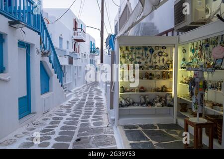 Mykonos, Cicladi, Grecia. 20 maggio 2021. Negozio di souvenir di arte greca acciottolato vuoto vicolo strette case bianche con porte finestre blu. Estate mattina Foto Stock